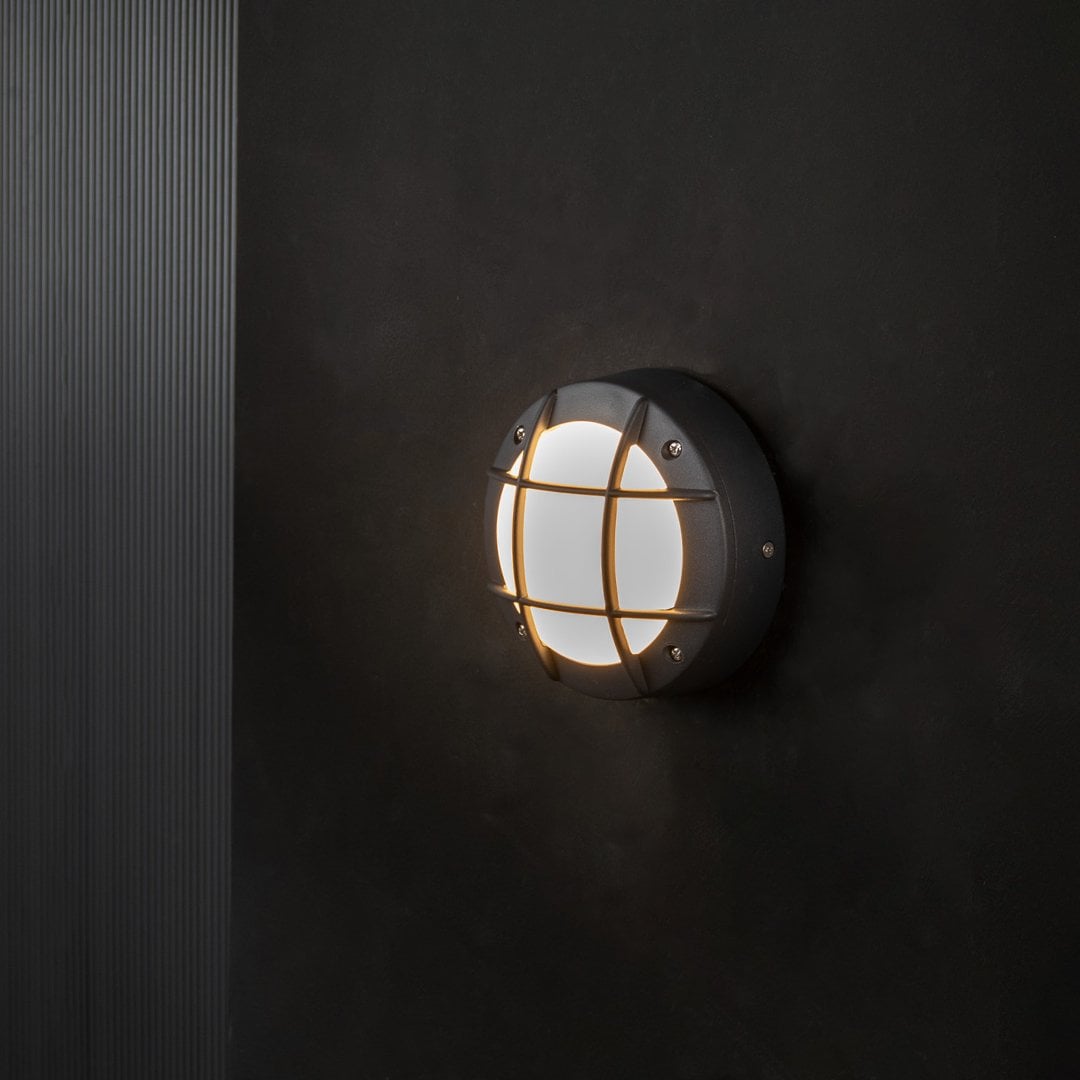 Round outdoor wall light with soft warm glow and black metal frame shown on black background for elegant lighting style.
