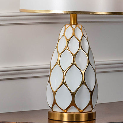 Closeup of ceramic table lamp with gold lattice design and white shade showing luxury detailing for modern decor lighting.