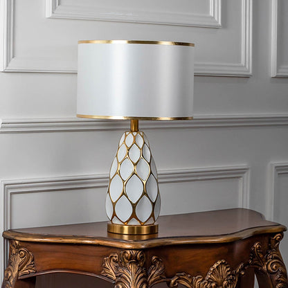 Gold ceramic table lamp with white shade switched off on white background for minimalist modern bedroom decor lighting.