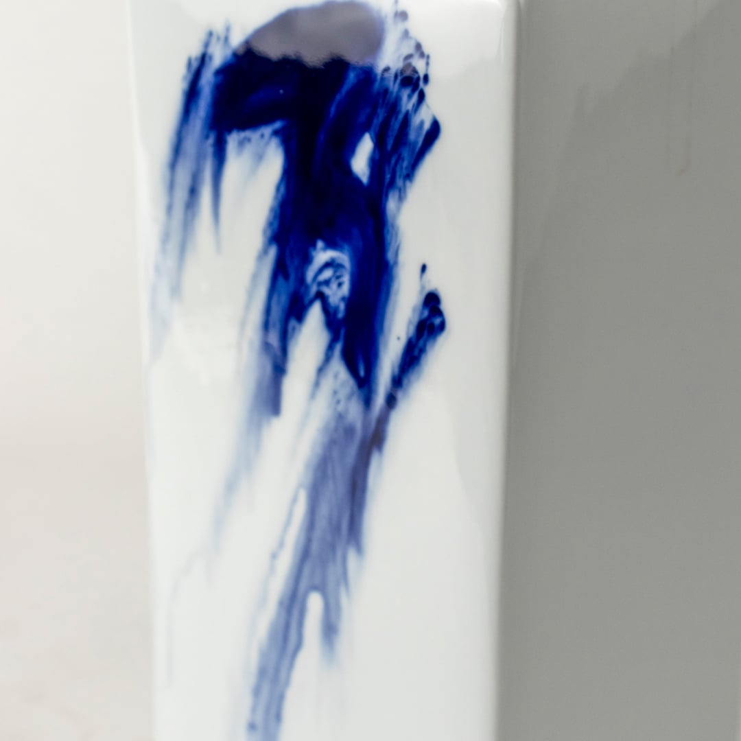 Tall white ceramic jar with vivid blue abstract brush design captured on smooth background for décor accents.