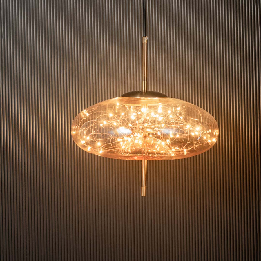Amber glass wide dome pendant ceiling light glowing warmly with filament design against black background creating luxury style.