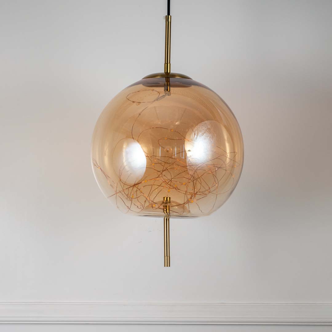 Elegant amber glass and gold globe pendant ceiling light displayed against off white background with modern round design.