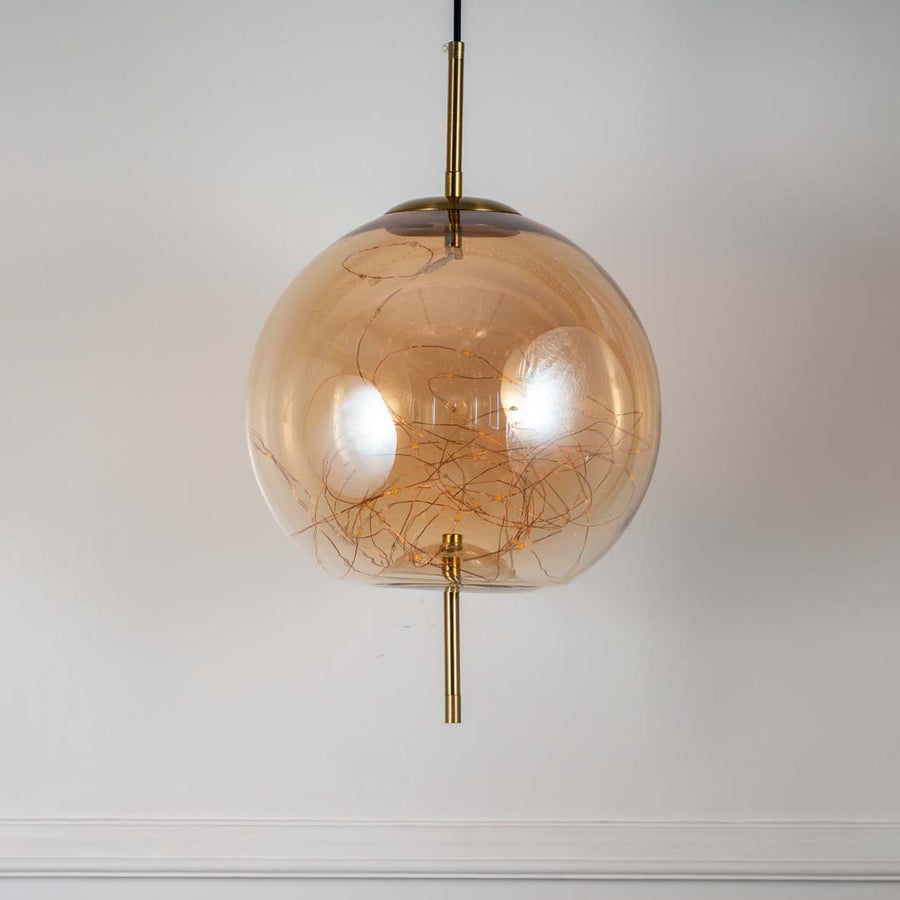 Elegant amber glass and gold globe pendant ceiling light displayed against off white background with modern round design.