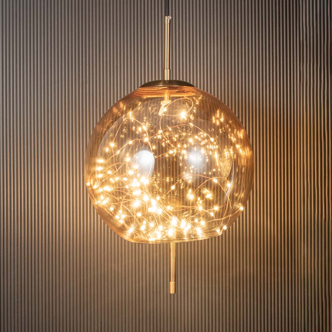 Amber glass globe pendant ceiling light glowing beautifully with warm filament lights against dark black background decor.