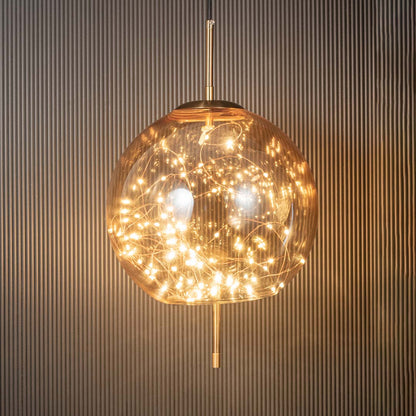 Amber glass globe pendant ceiling light glowing beautifully with warm filament lights against dark black background decor.