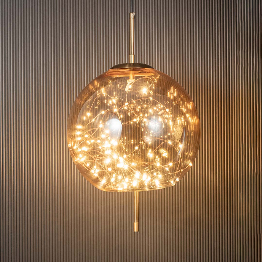 Amber glass globe pendant ceiling light glowing beautifully with warm filament lights against dark black background decor.