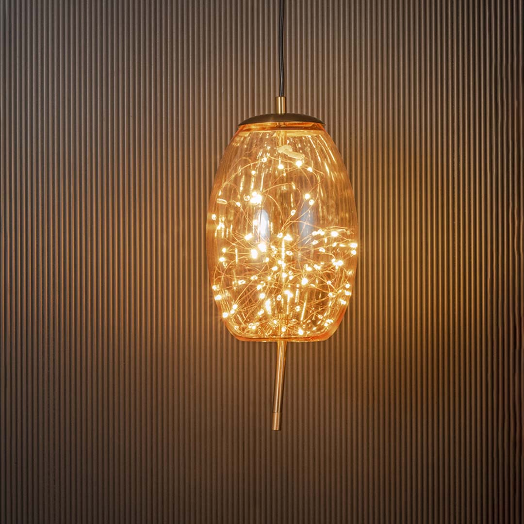Amber glass and gold pendant ceiling light glowing warmly with filament design illuminated beautifully on black background.