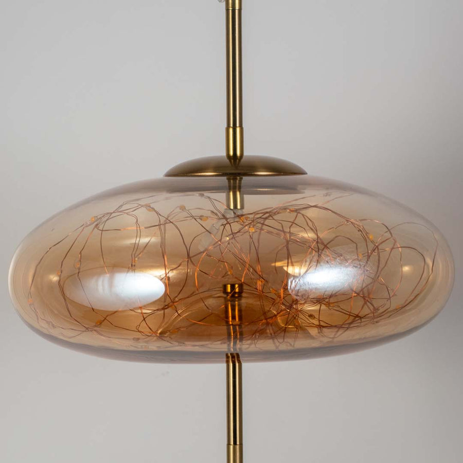 Closeup of amber glass pendant light with artistic wire detailing showcasing luxurious craftsmanship.
