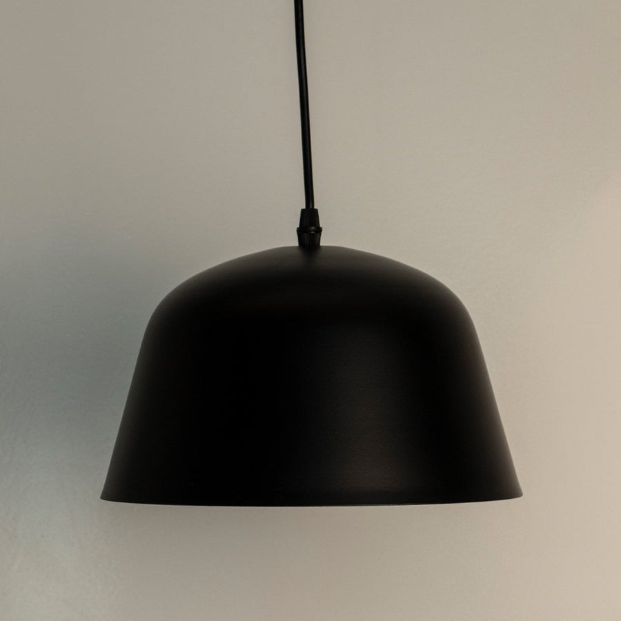Matte black dome pendant light turned on against white background creating stylish focal point in contemporary room with soft ambient lighting.