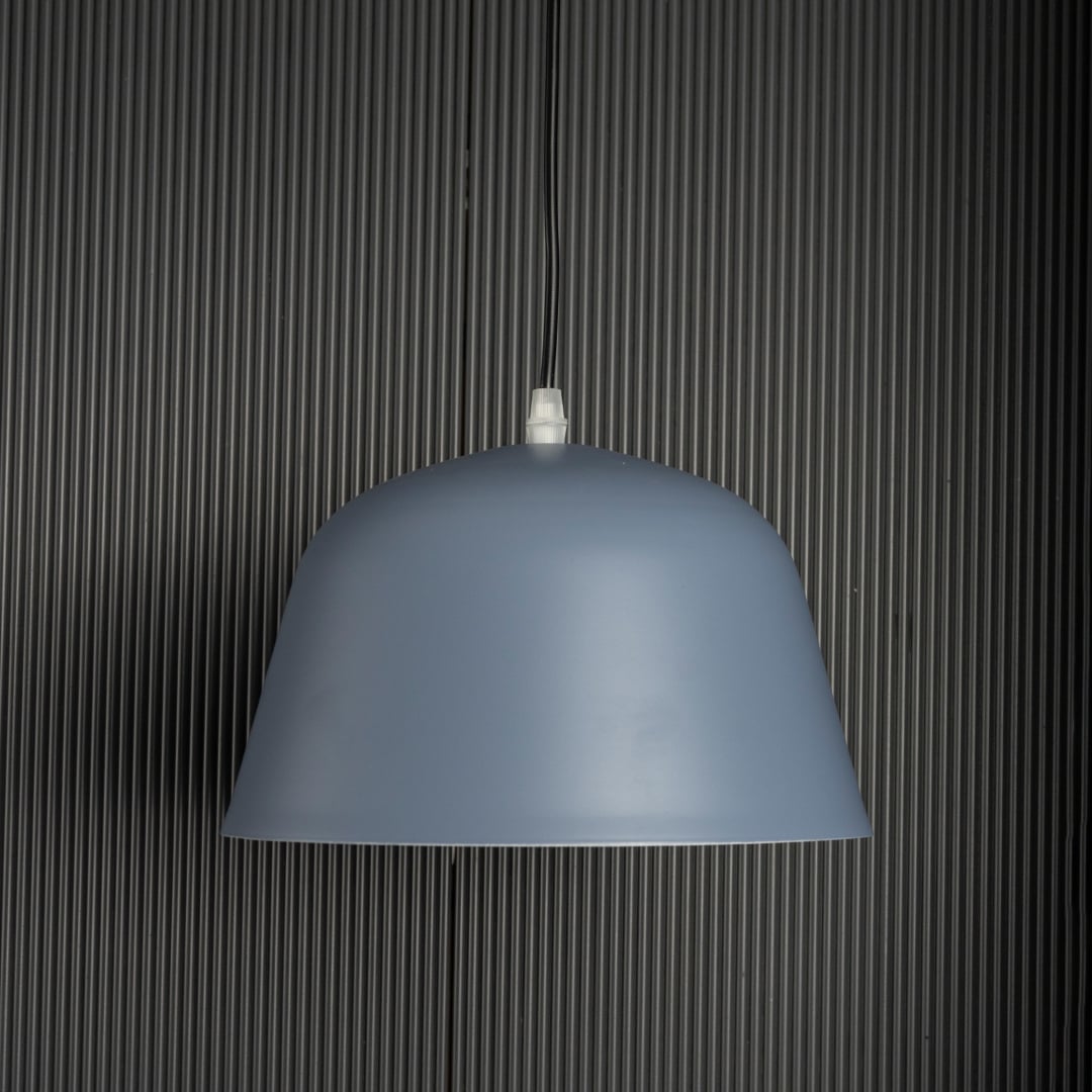 Matte blue dome pendant light turned off against dark ribbed background highlighting its smooth surface and clean form.