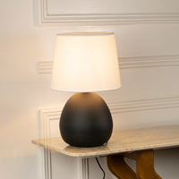 Black ceramic table lamp with white fabric shade casting warm ambient light for elegant bedside and living room decor.