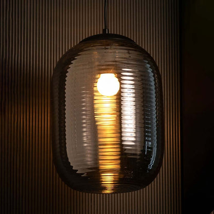A contemporary ribbed smoked glass pendant light glowing warmly against a dark textured backdrop creating a rich ambient lighting effect for interiors.