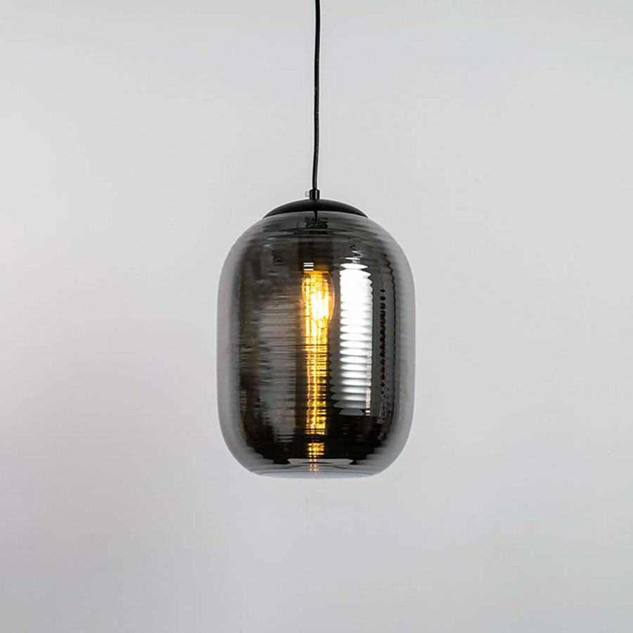 A ribbed smoked glass pendant light shown with light on against a white background highlighting its warm glow and tall rounded contemporary shape.