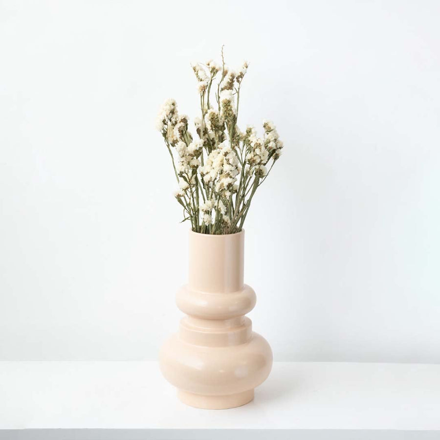 Modern peach ceramic vase placed on a white platform with patterned wall backdrop  emphasizing its elegant curves and tall silhouette.