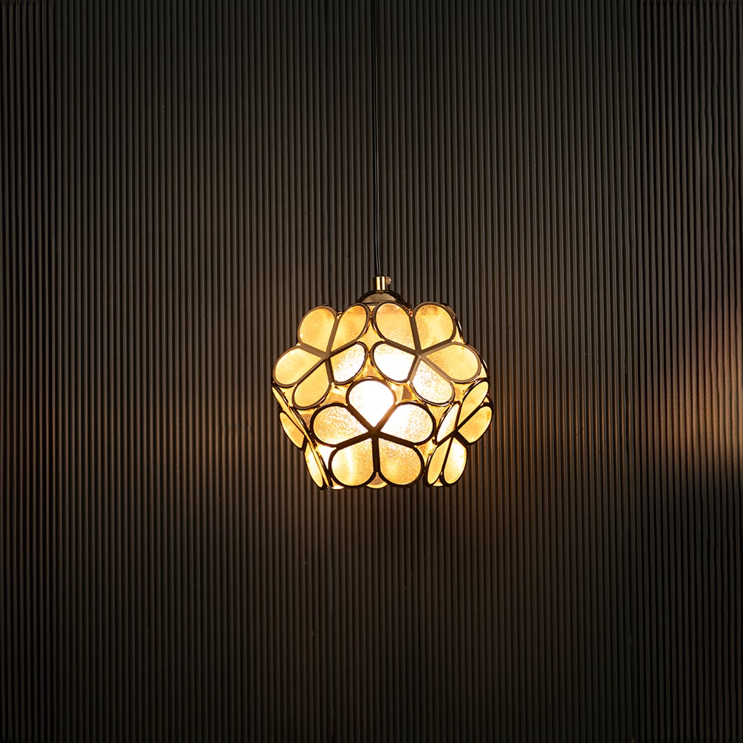 Elegant gold floral pendant light illuminated on dark background showcasing its artistic handcrafted metal design.