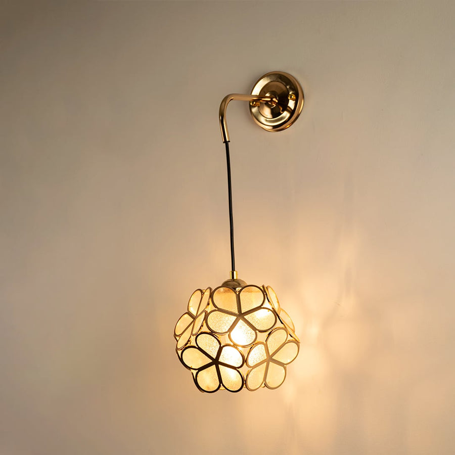 Artistic gold wall light with floral metal frame glowing softly on white background creating warm ambience.