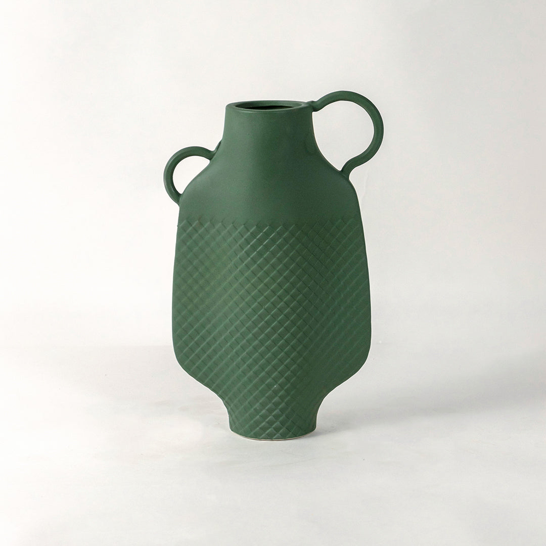 Green ceramic vase with dual side handles and textured surface placed on white surface against neutral background enhancing contemporary home decor aesthetic.