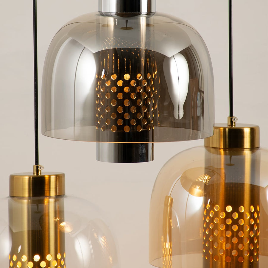 Close up of three pendant lights with smoky clear and amber dome glass shades each showing a glowing perforated gold inner cylinder.