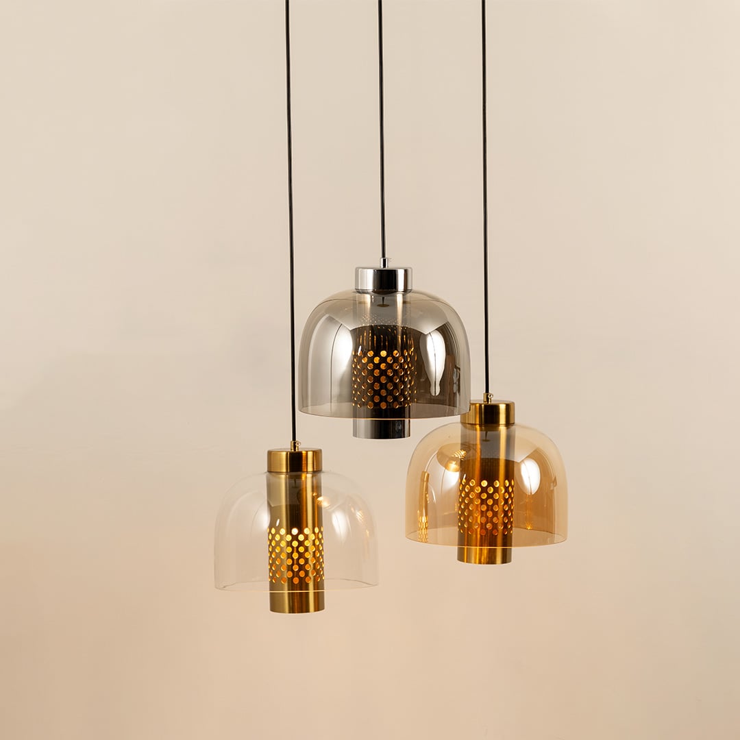 Three hanging pendant lights with dome glass shades in clear smoky and amber tones each with a perforated gold inner cylinder glowing softly.