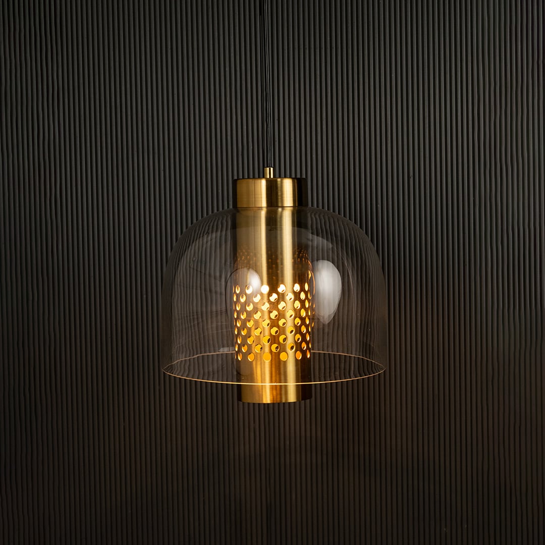 Clear glass pendant with perforated metal cylinder casting warm ambient light imagined against a dark background creating a dramatic modern interior decor effect.