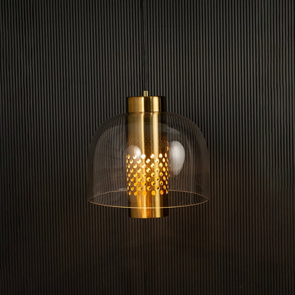 Clear glass pendant with perforated metal cylinder casting warm ambient light imagined against a dark background creating a dramatic modern interior decor effect.