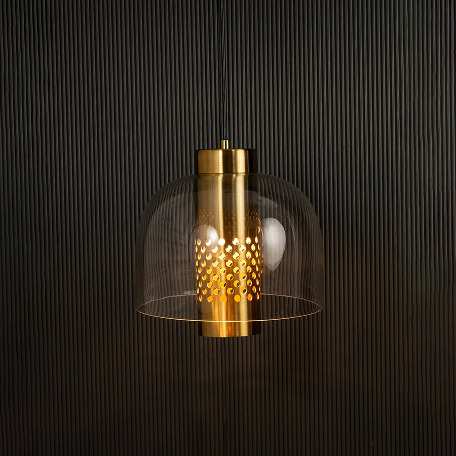 Clear glass pendant with perforated metal cylinder casting warm ambient light imagined against a dark background creating a dramatic modern interior decor effect.