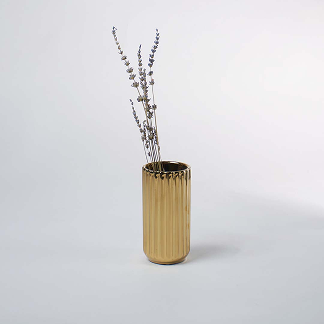 A shiny gold vase with a ribbed texture displayed in a soft minimal setting creating a warm elegant lifestyle look that highlights its modern charm.