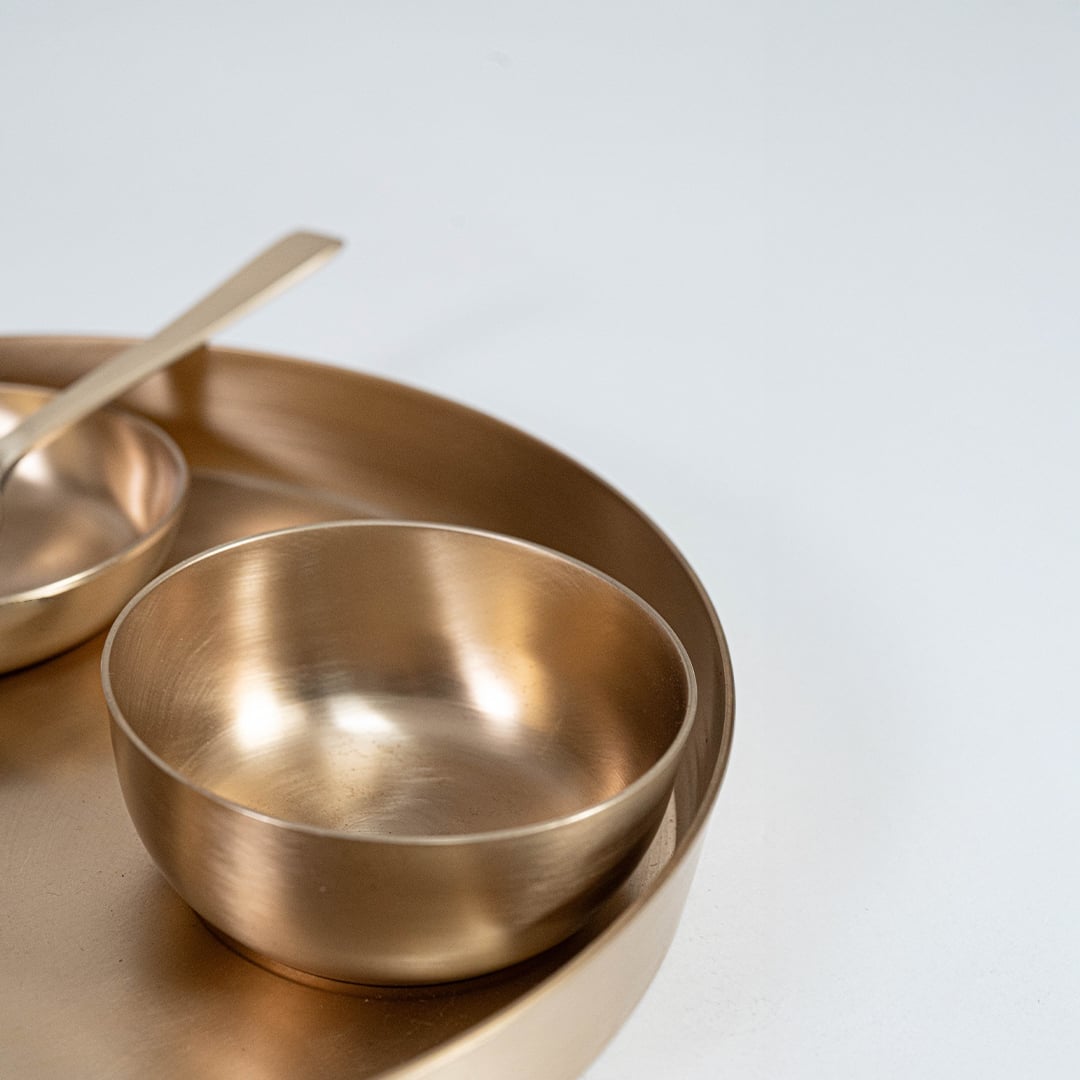 Traditional Indian meal served in brass thali set with rice curry raita and naan placed on rustic wooden table.