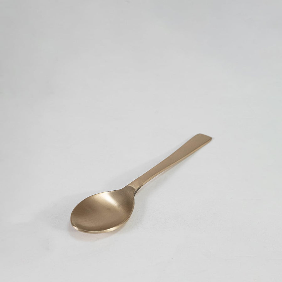 Brass spoon with curved bowl and simple flat handle design shown on plain white background for utensil detail.