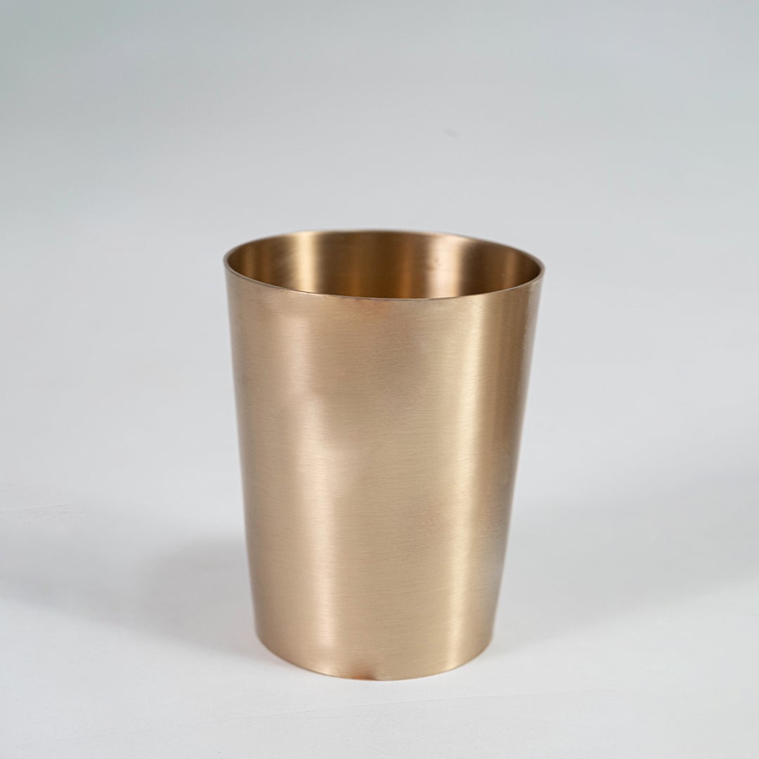A brass cup shown on a white background highlighting its smooth metallic finish and simple cylindrical shape designed for everyday serving use.