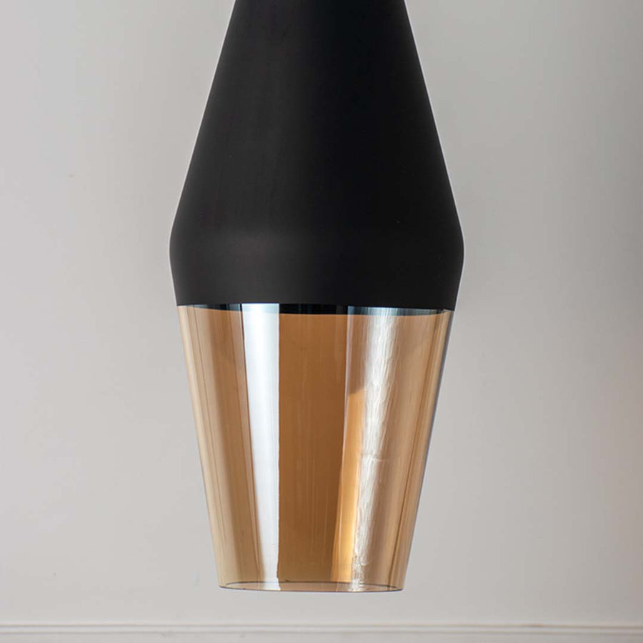 Closeup of black metal pendant light with amber glass diffuser showcasing premium craftsmanship and elegance.