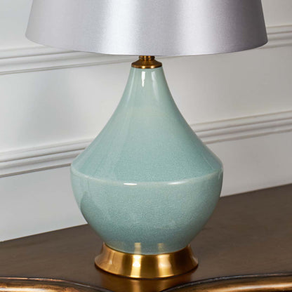 Detailed closeup of green table lamp showcasing smooth ceramic texture gold accent base and premium fabric lampshade craftsmanship.