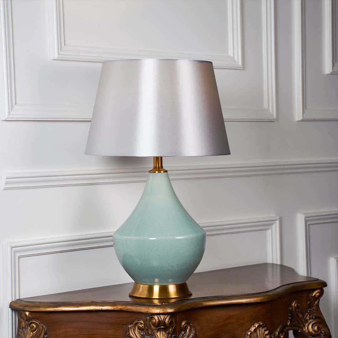 White fabric shade table lamp with glossy mint ceramic base and gold accent casting warm ambient light on side table.