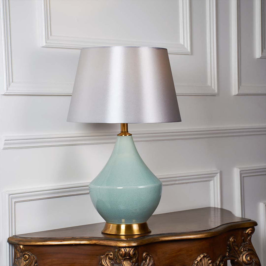 White fabric shade table lamp with glossy mint ceramic base and gold accent casting warm ambient light on side table.
