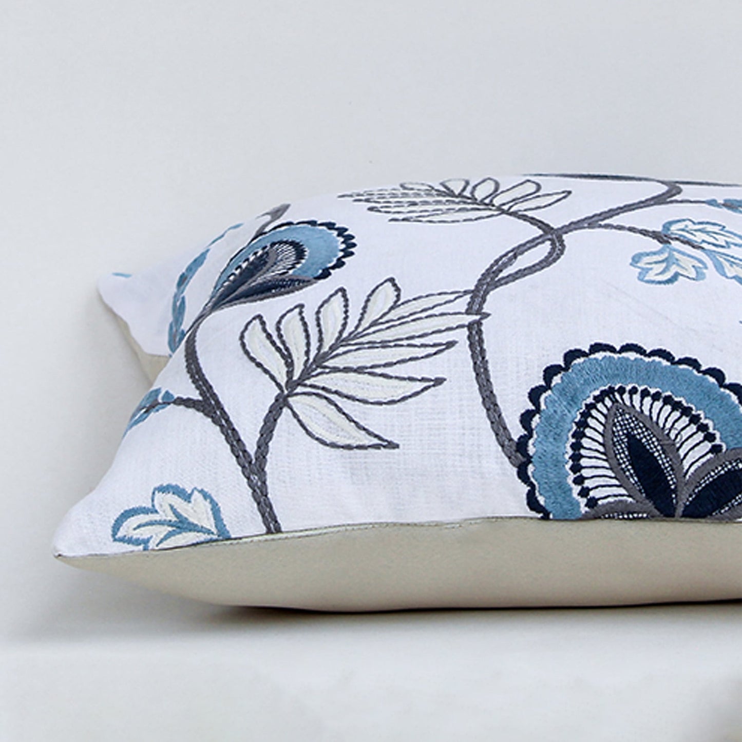 Soft cotton cushion cover with blue floral embroidery shown at an angle adding a fresh nature inspired décor element with a breathable smooth and skin friendly fabric suitable for modern interiors.