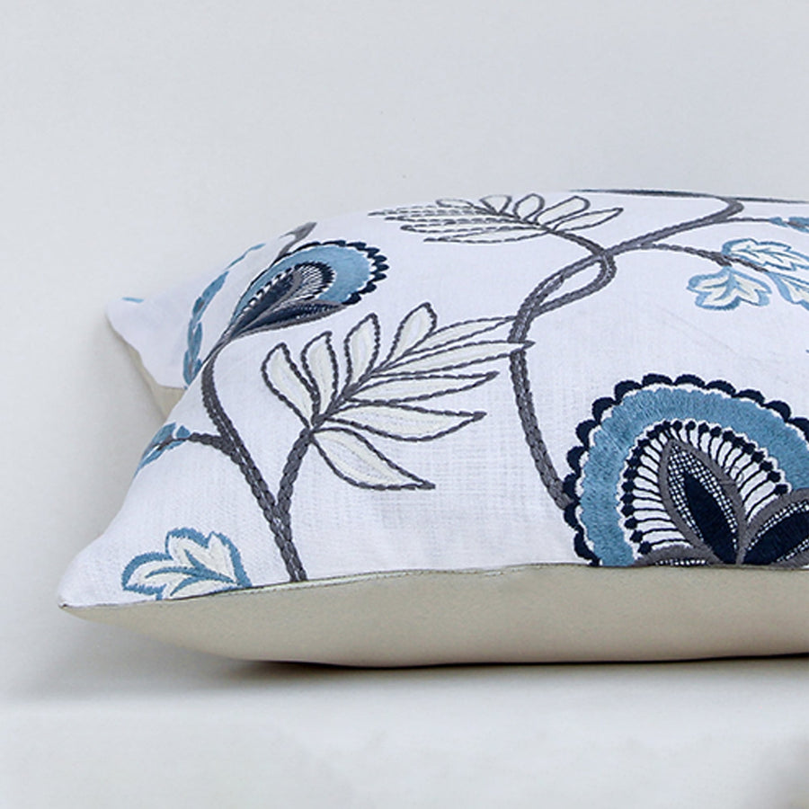 Soft cotton cushion cover with blue floral embroidery shown at an angle adding a fresh nature inspired décor element with a breathable smooth and skin friendly fabric suitable for modern interiors.