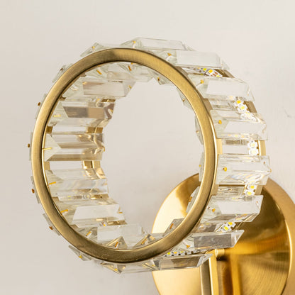 A closeup of a round wall light with textured clear glass and gold metal glowing brightly against a soft neutral background showcasing refined artistic décor.