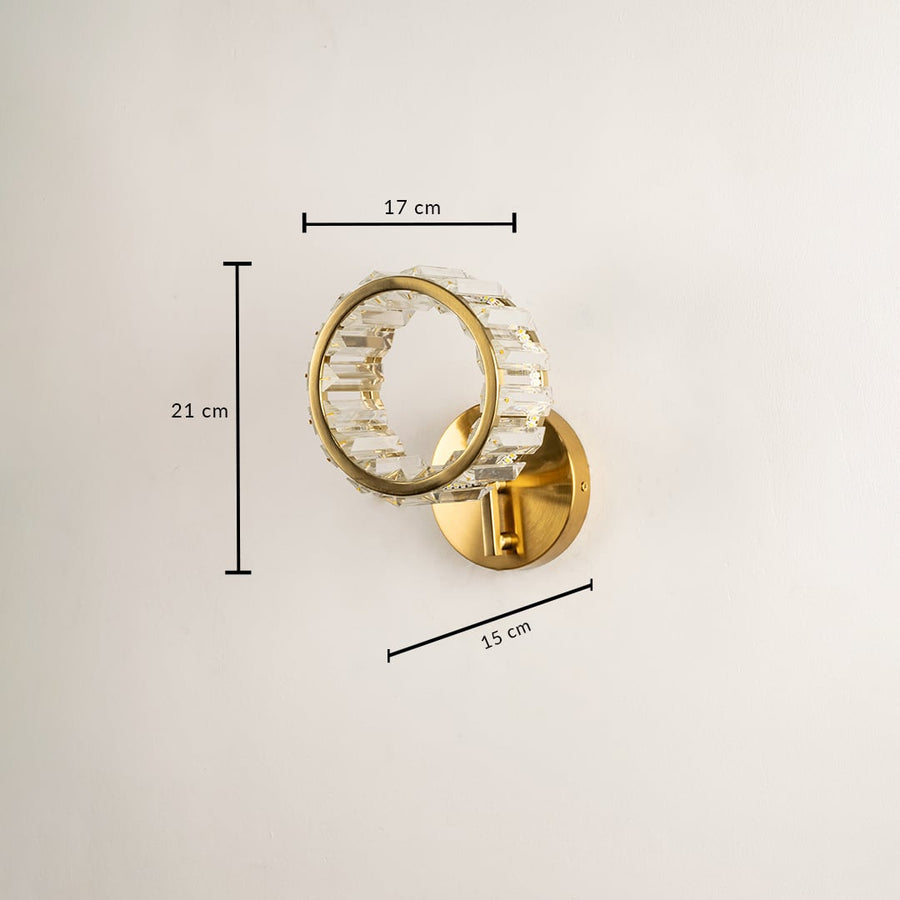 A glass and gold metal wall light with the light off mounted on a dark ribbed background showcasing its sculptural form and adding bold artistic contemporary décor.
