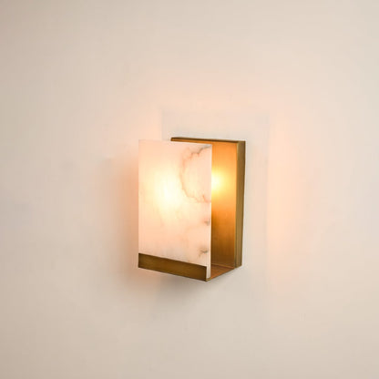 Rectangular metal wall sconce illuminated on white background featuring alabaster texture and warm glow perfect for refined and elegant interiors.