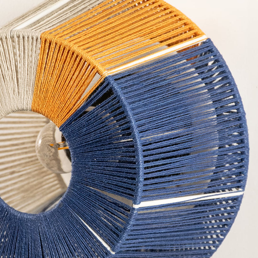Detailed macro view of a contemporary woven thread wall light fixture showcasing textured blue yellow and cream cotton cords.