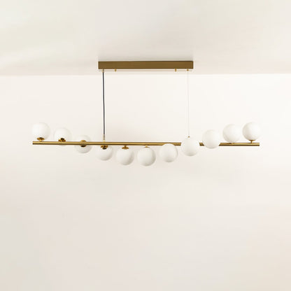 Gold linear chandelier with staggered white globes in a front view against a white background with lights on ideal for modern lighting décor.