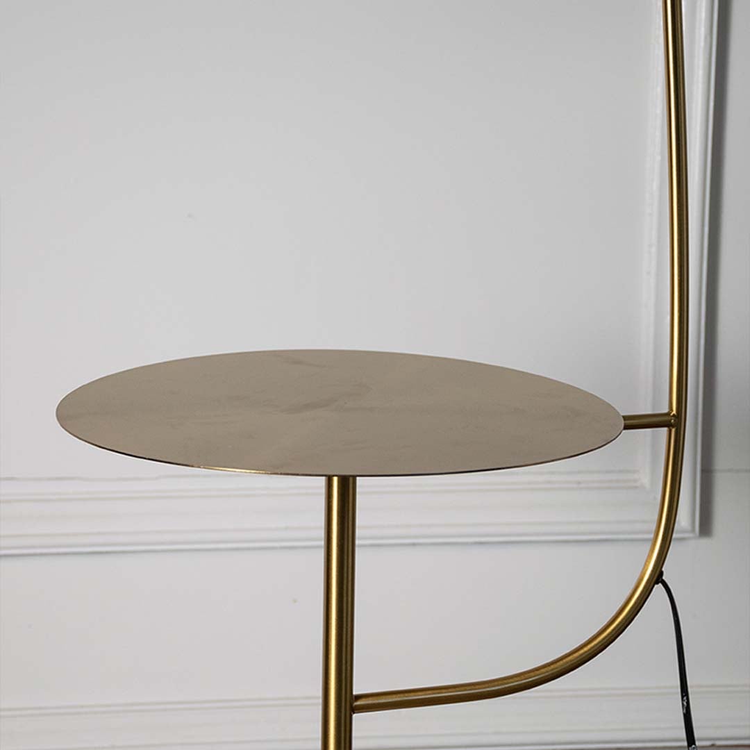 Closeup of gold floor lamp with cylindrical shade and side table showing sleek metallic finish.