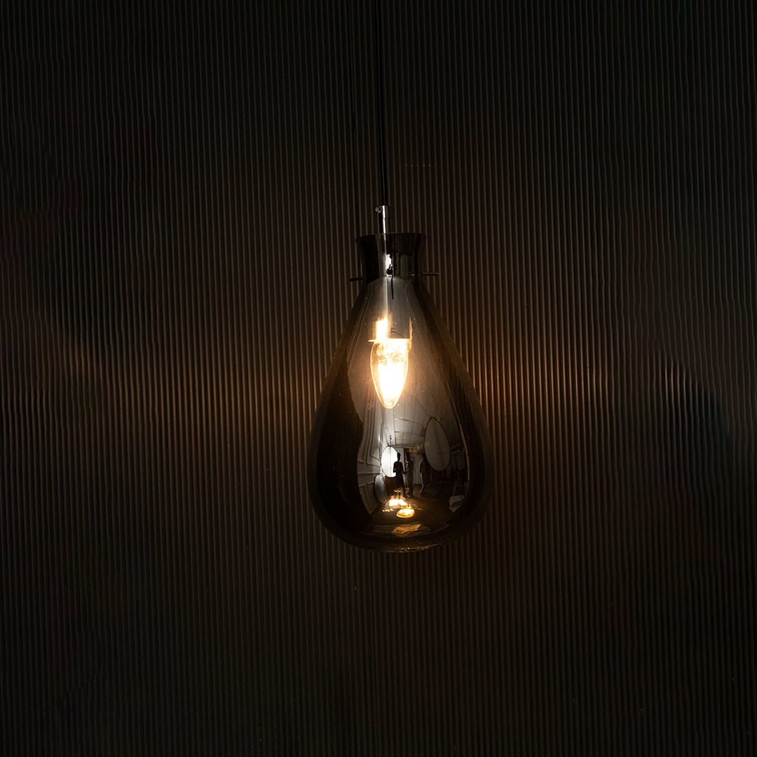 Elegant smoked chrome glass pendant light illuminated beautifully on dark background highlighting its artistic shape and glossy finish.