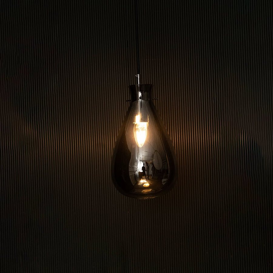 Elegant smoked chrome glass pendant light illuminated beautifully on dark background highlighting its artistic shape and glossy finish.