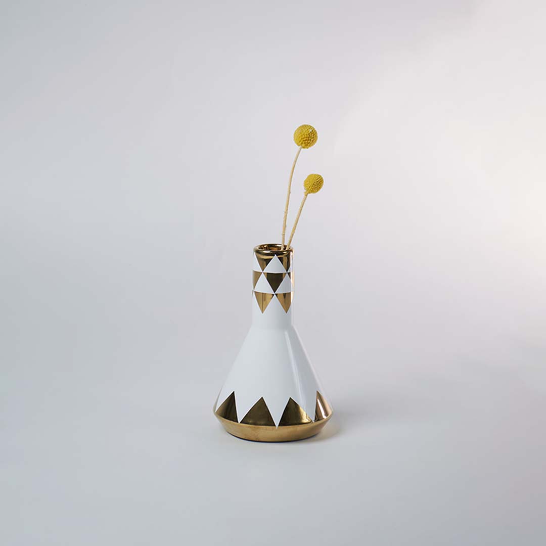 Stylish white and gold ceramic vase with geometric patterns placed with minimal decor in a bright modern setting.
