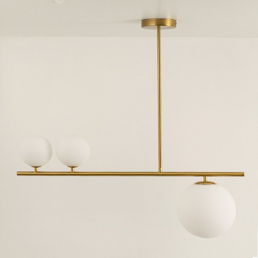 Gold linear chandelier displayed with lights off showing sleek frame frosted glass globes and modern minimalistic aesthetic design.