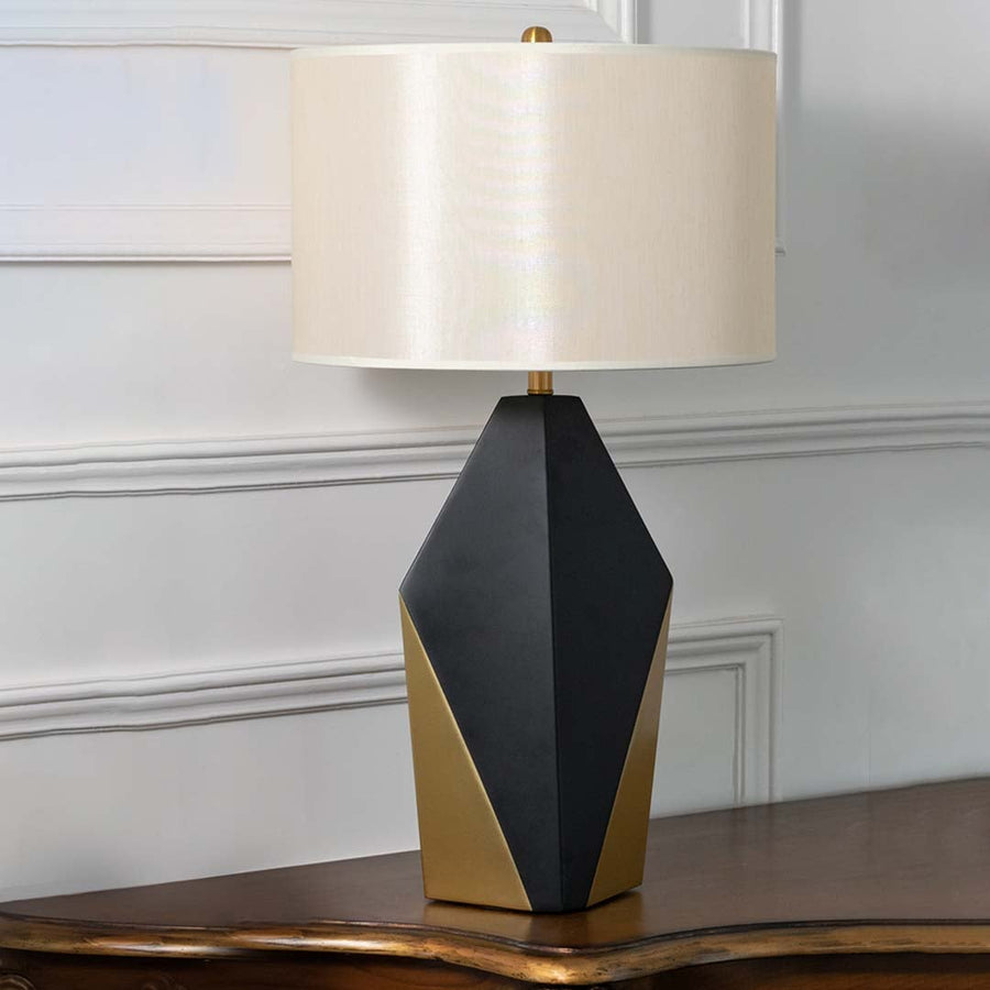 Black and gold geometric table lamp with white drum shade and faceted base displayed on a white background perfect for stylish contemporary interiors.