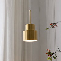 Minimalist gold brass cylinder pendant light fixture hanging against white curtains for contemporary home dining room decor.