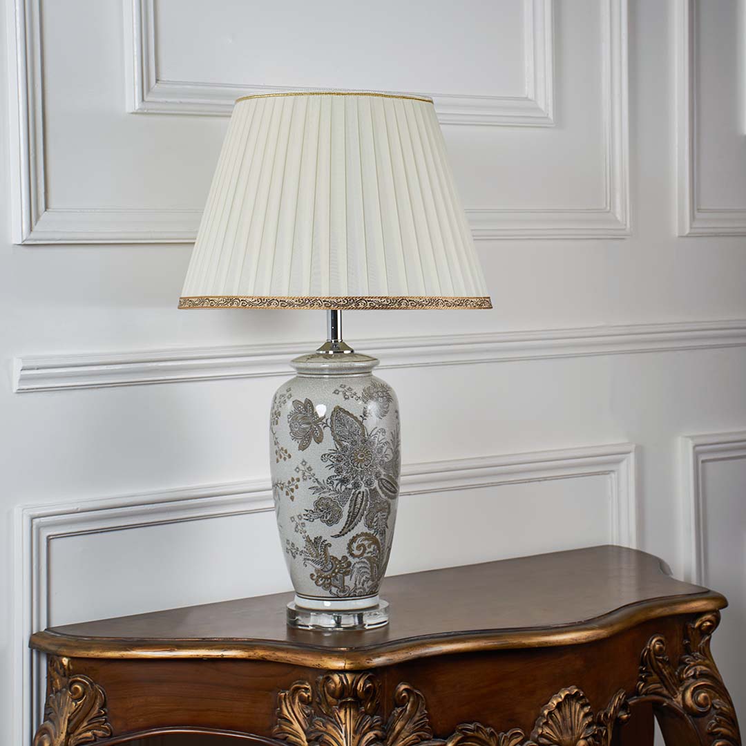 Decorative ceramic table lamp with floral artwork and pleated shade shown on a clean white background with soft neutral tones.
