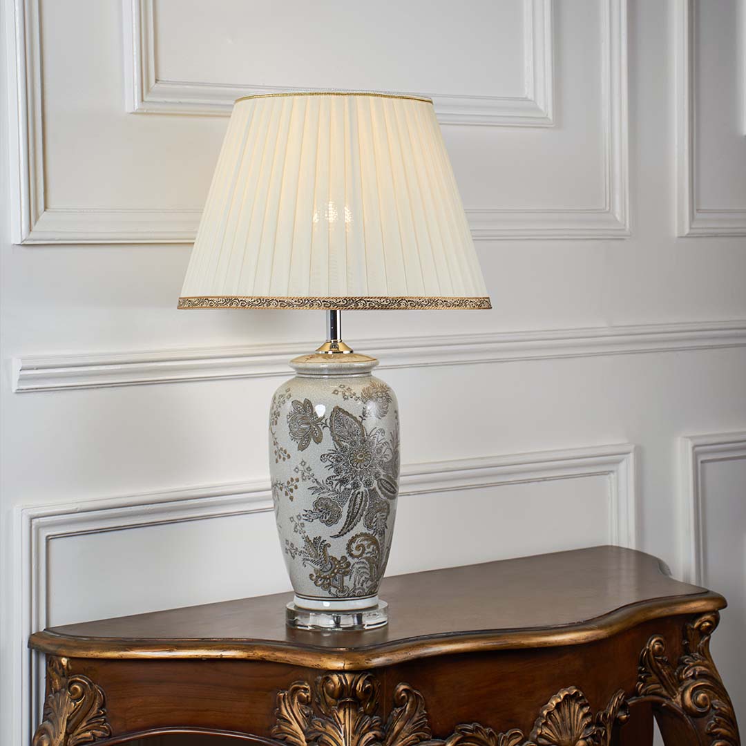 Grey floral ceramic table lamp with pleated fabric shade offering timeless traditional style and warm ambient lighting.